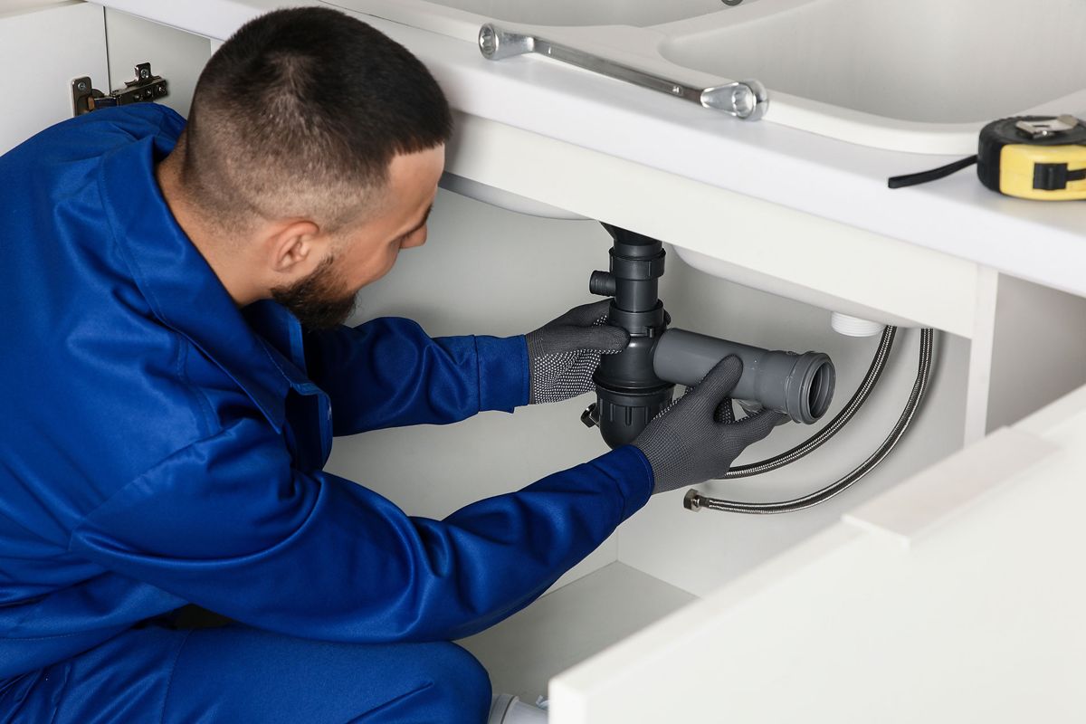 Plumber repairing the drain pipe under a kitchen sink