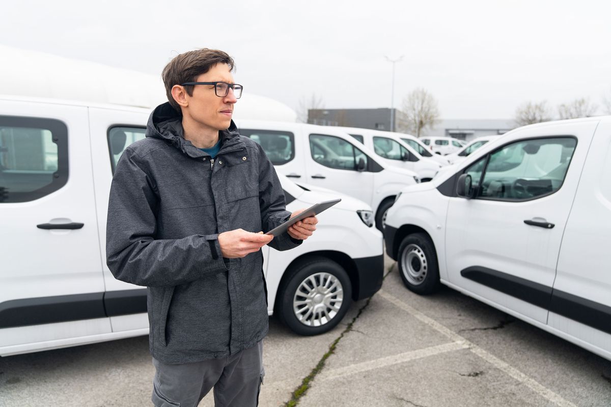 Fleet manager with a tablet beside a row of white service vans